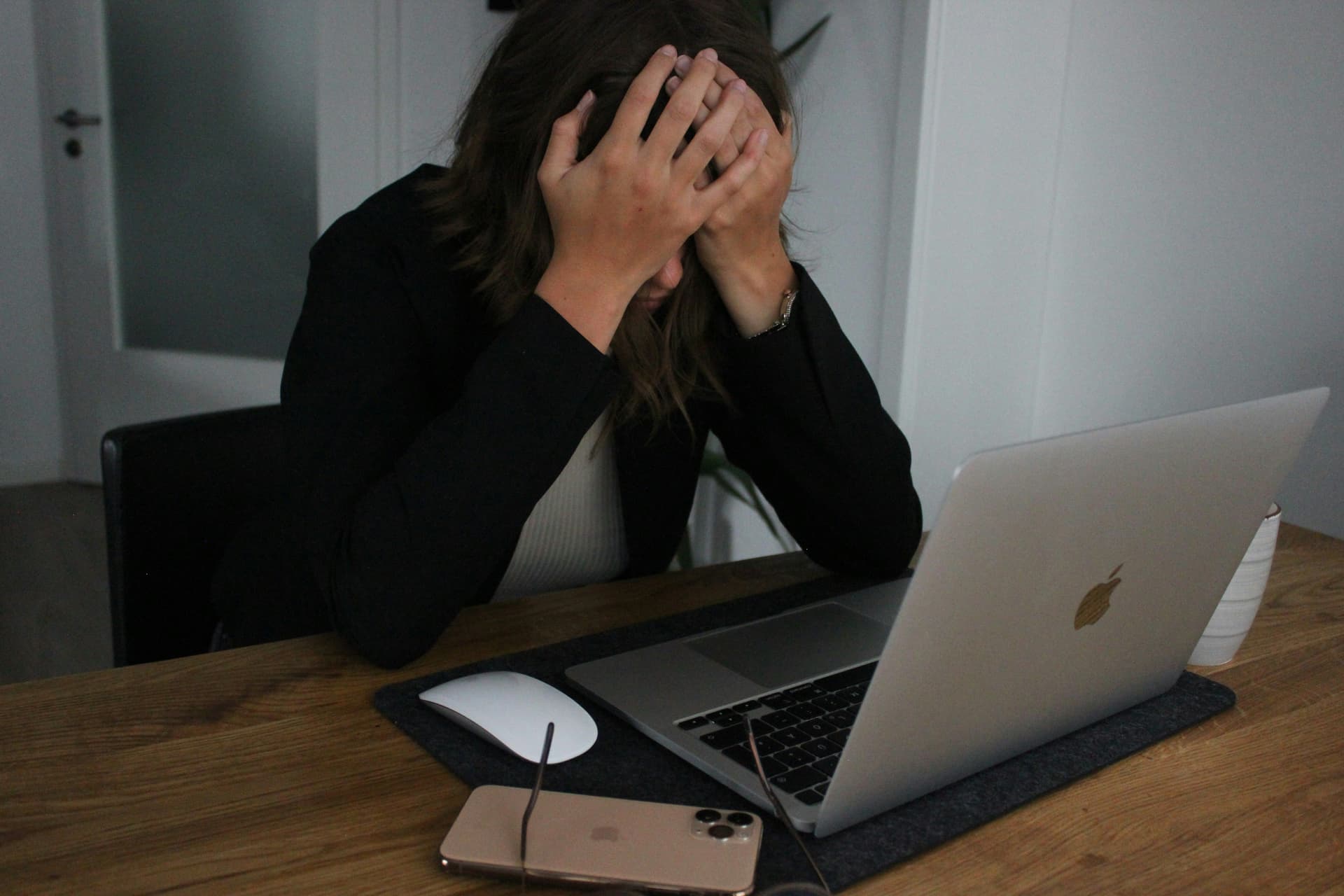 Stressed person sitting at a desk with head in hands, laptop in front, overwhelmed