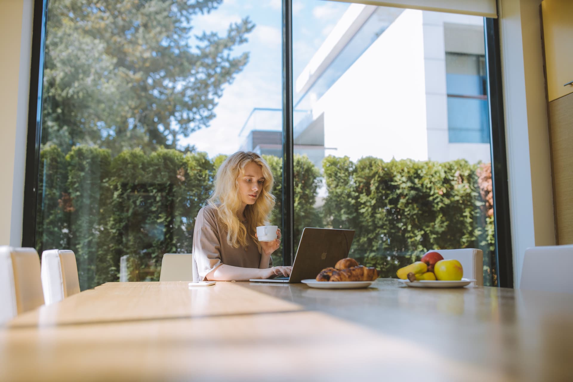 oman working at a table by a large window with a cup of coffee