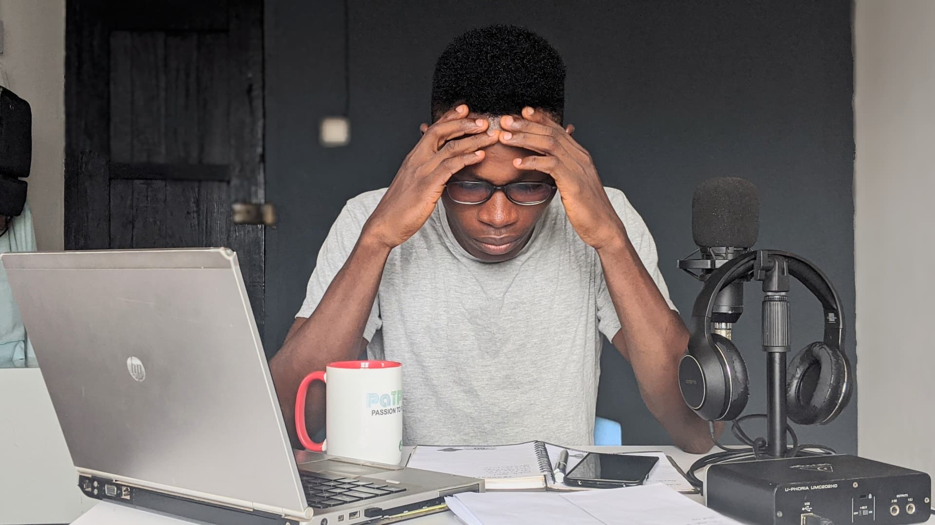 Man with his hands on his head at a home desk with a laptop and notebook
