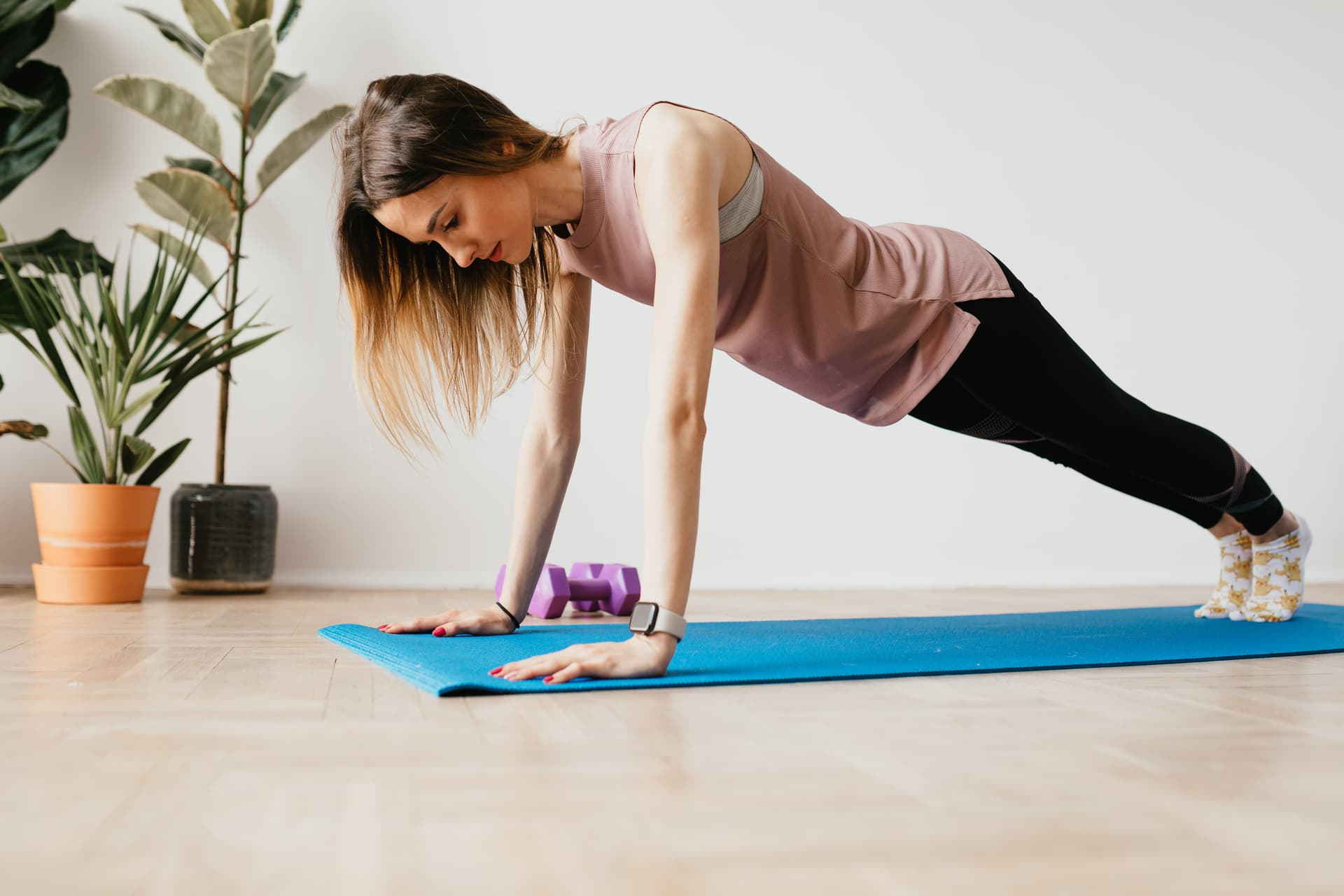 Woman doing a plank on a blue yoga mat in a bright living room
