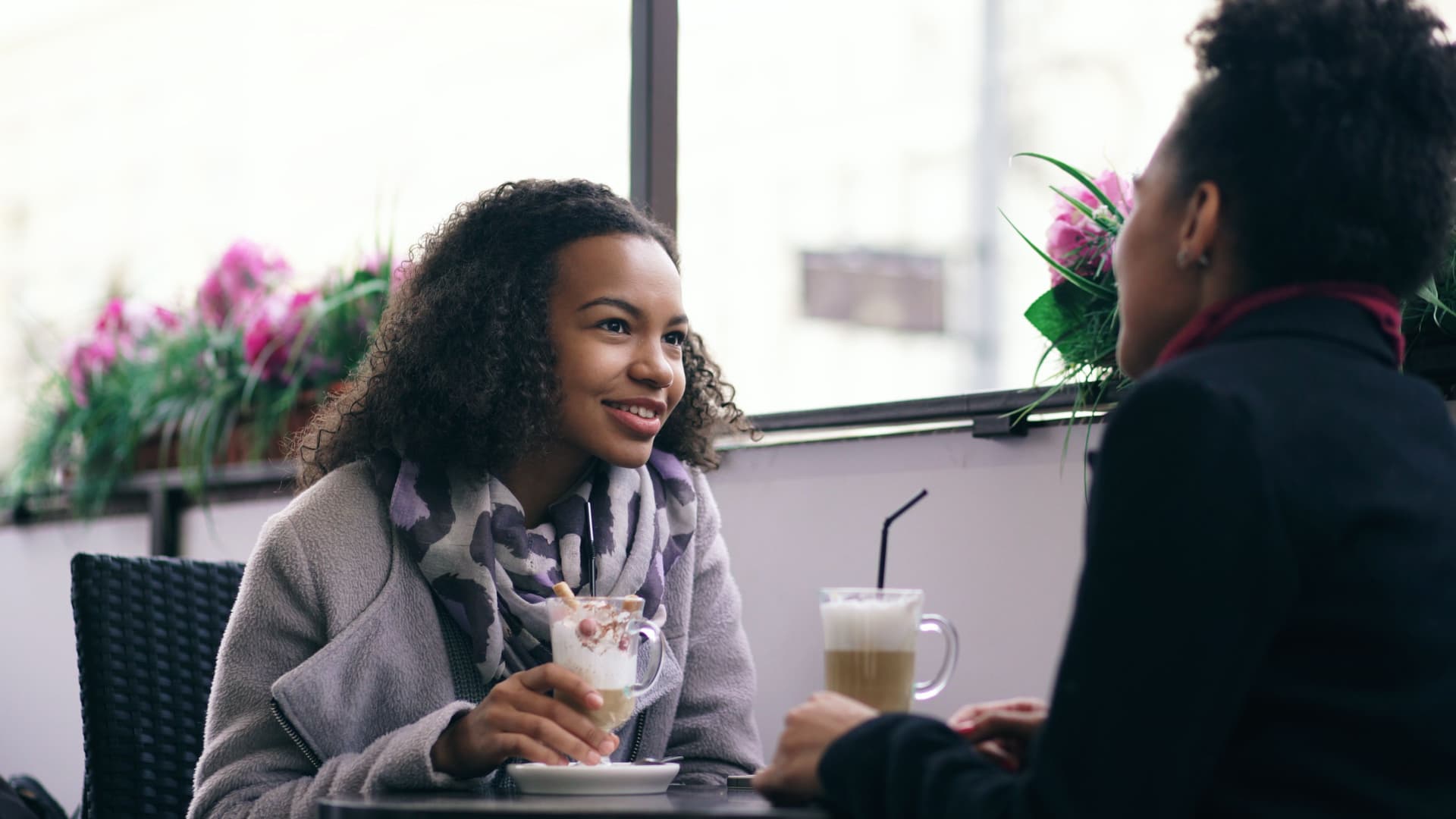 Two women talking and smiling over coffee at a café table