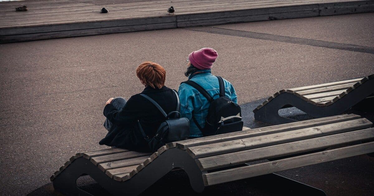 Two women sitting together on a park bench, sharing a quiet moment of support and understanding