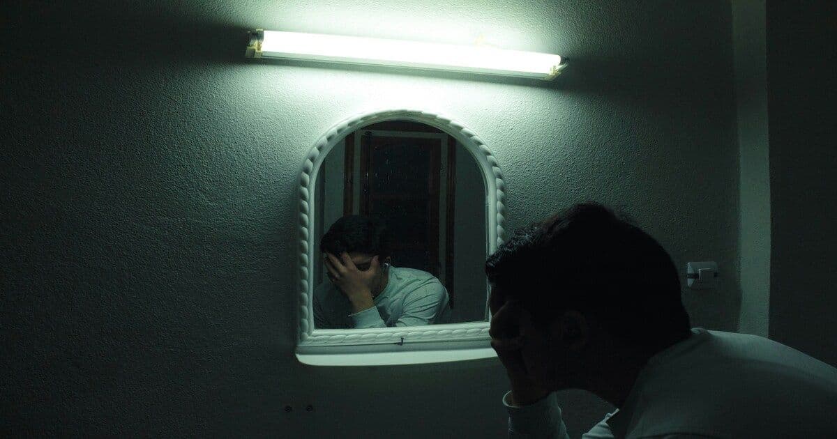 Person looking at themselves in the mirror with a worried or reflective expression, representing mental health struggles.
